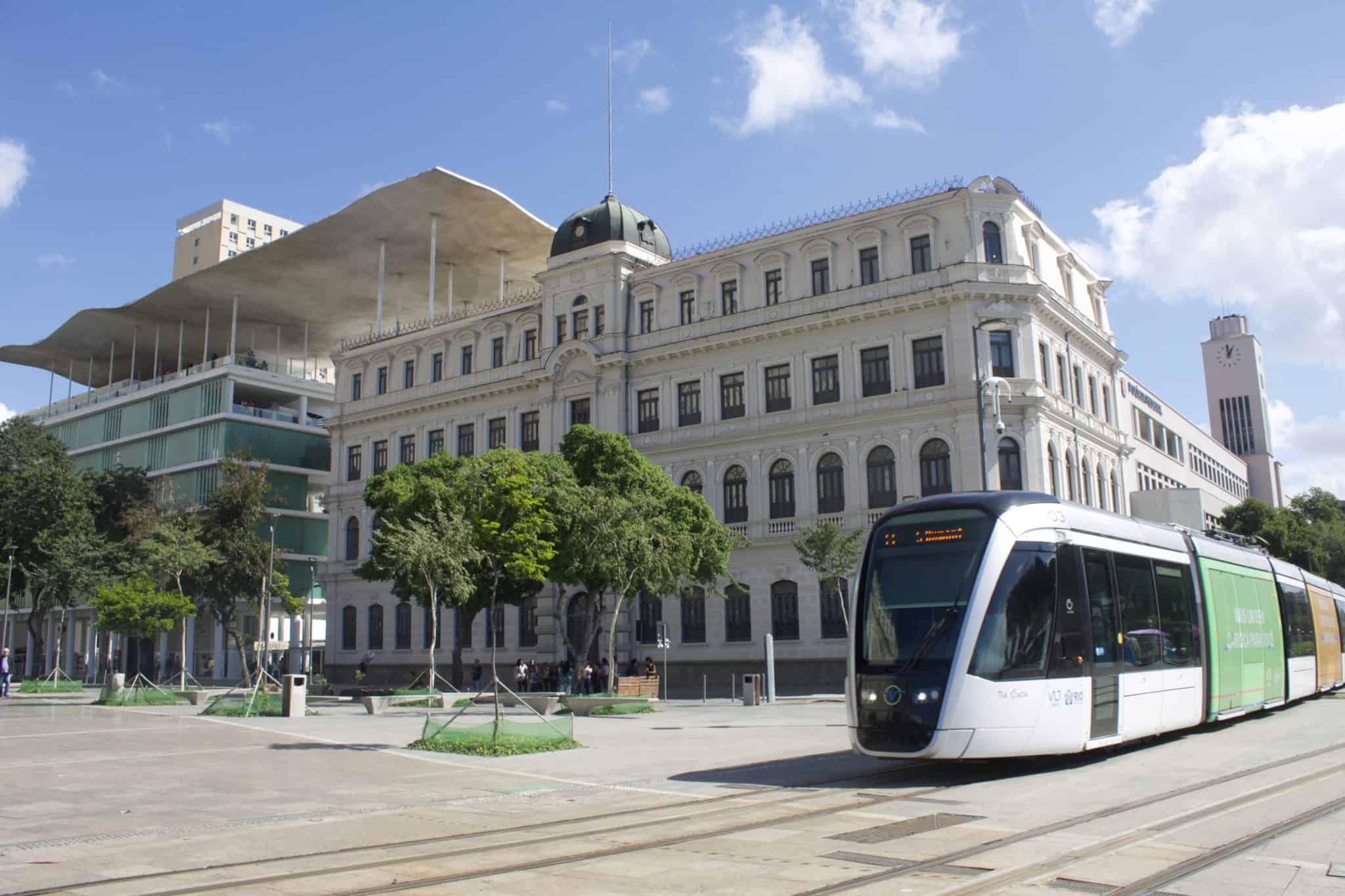 Fachada externa com prédio histórico e VLT passando em frente.