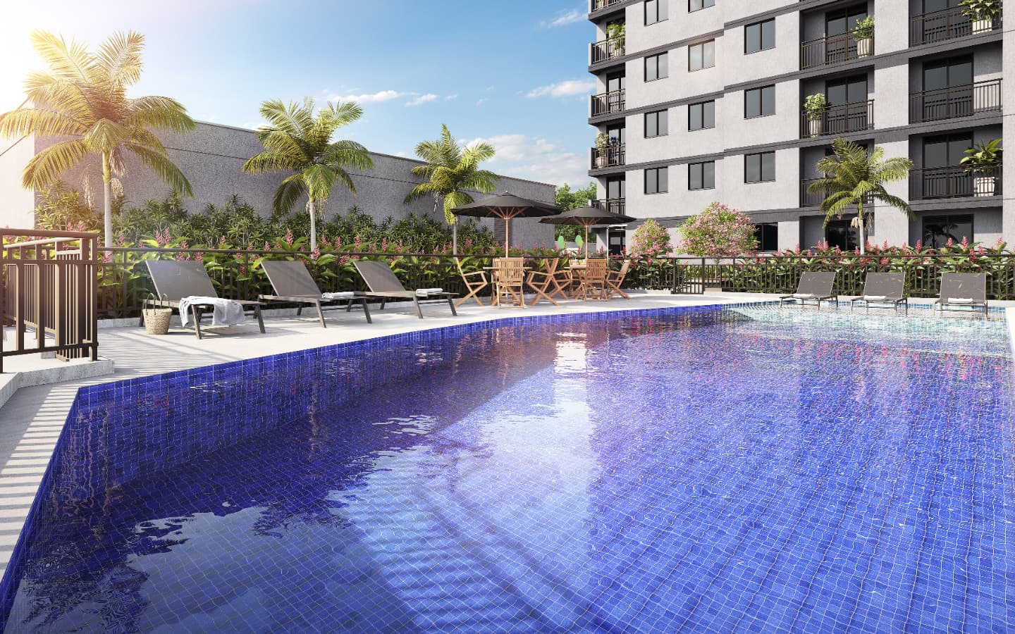 Piscina com revestimento azul, espreguiçadeiras e mesas com guarda-sol em área externa.