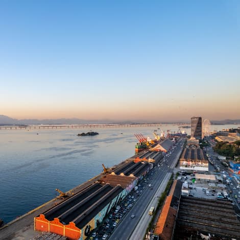 Vista aérea da região portuária com mar, galpões e edifícios ao entardecer.