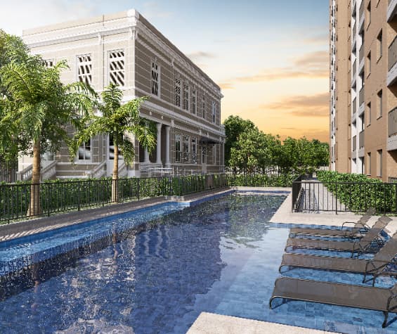 Piscina com espreguiçadeiras, ao lado de um edifício histórico e área verde.