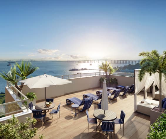 Terraço com espreguiçadeiras, mesas, guarda-sol e vista para o mar.